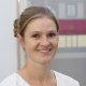 Porträt von Jenny Schärer, Dentalassistentin EFZ in der Zahnarztpraxis Spitalgasse in Bern. Die Frau mit zusammengebundenem Haar trägt eine weisse Berufskleidung und lächelt freundlich in die Kamera.