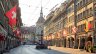 Blick durch die Berner Spitalgasse in der Altstadt mit Lauben, dem historischen Käfigturm im Hintergrund, geschmückten Schweizer und Berner Fahnen sowie einem Brunnen im warmen Abendlicht. Standort der Praxis Spitalgasse.